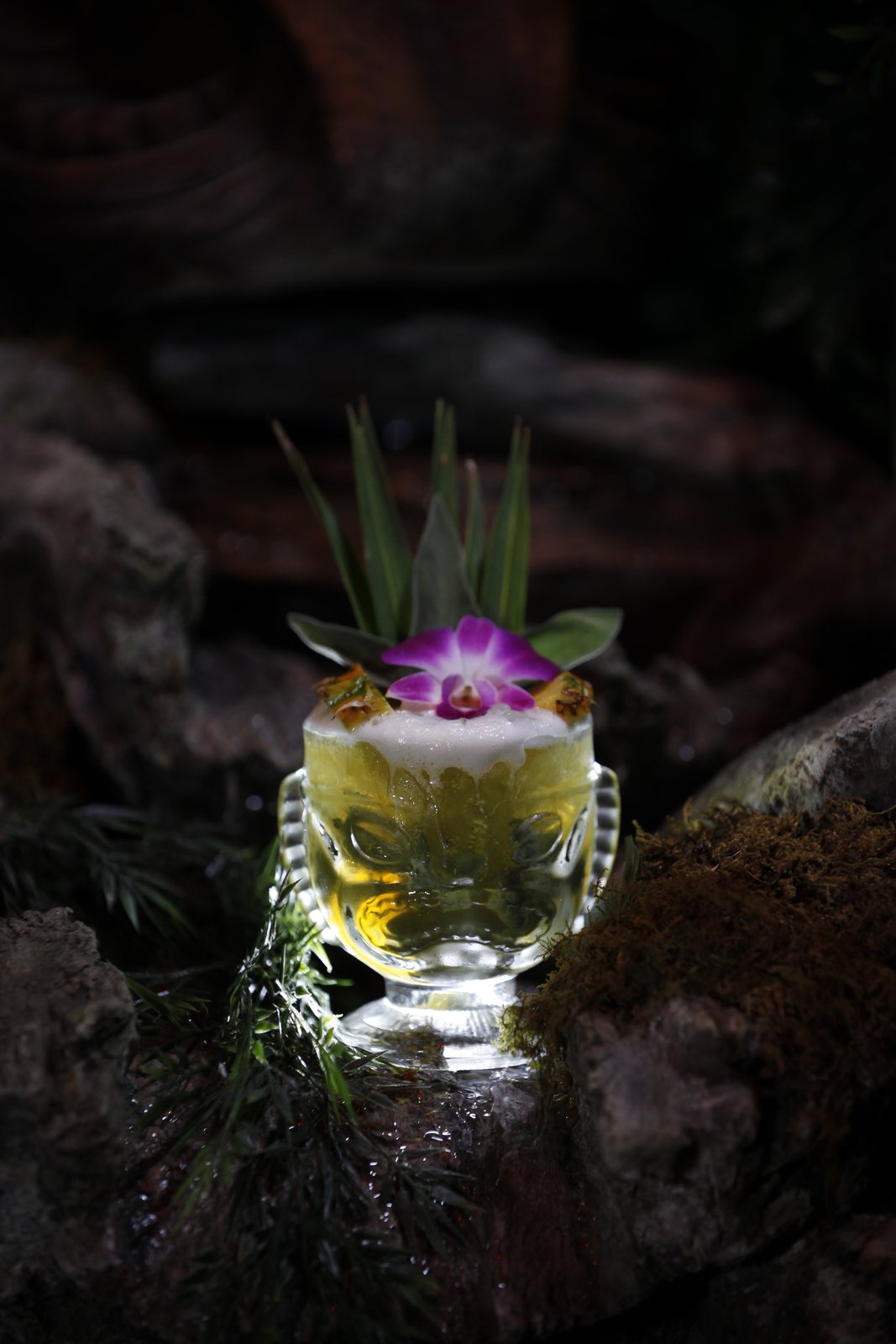 Tiki cocktail with an orchid, glowing among mossy rocks